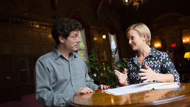 A group of two people seated at at table speaking to each other.